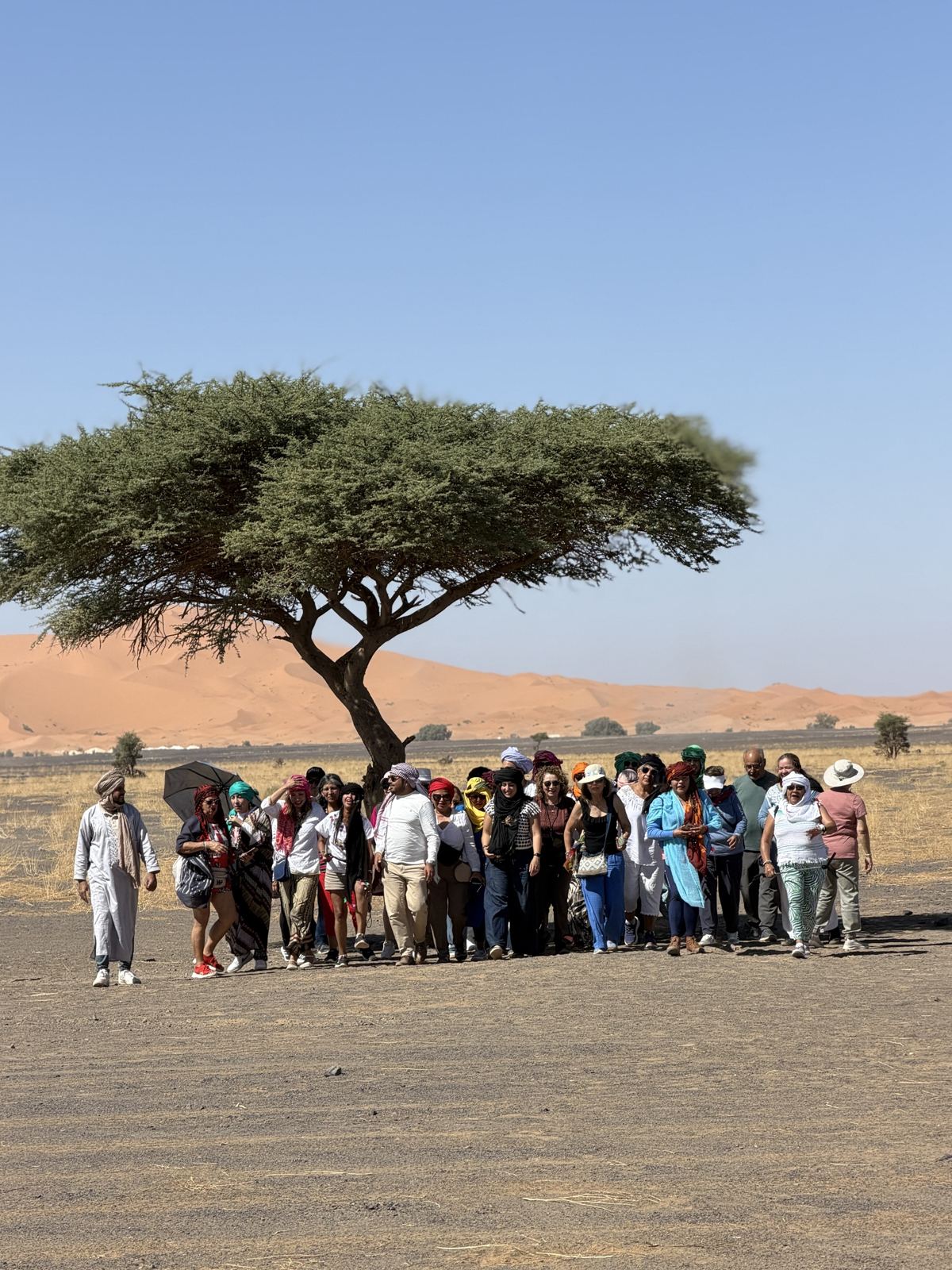 Grupo de viajeros caminando por el desierto frente a las dunas de Erg Chebbi